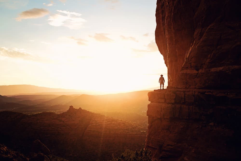 person standing on a ledge on the side of a cliff overlooking a sunset