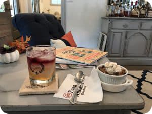 A dining table with a cocktail and a dessert dish next to a stack of books