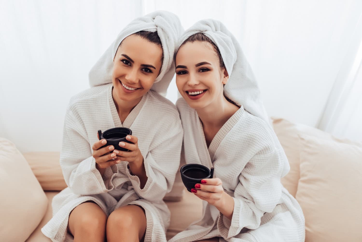 two women in robes with cups of coffee on a couch