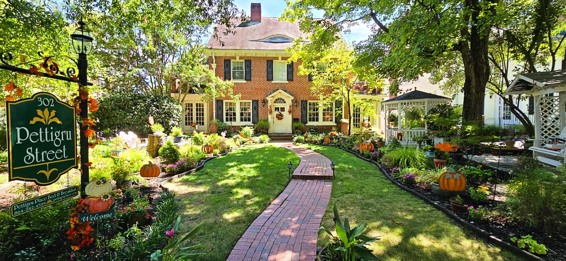 Front view of Pettigru Place Bed & Breakfast, a historic brick building surrounded by vibrant gardens, a brick pathway, and seasonal fall decorations, including pumpkins and autumn leaves