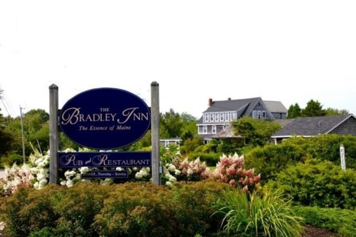 A view of the main inn building from the road with the navy blue Bradley Inn Sign in the foreground.  Pinky Winky Hydrangea in full bloom behind the sign