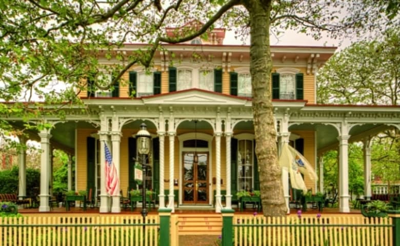 Victorian building in hues of yellow and green with tree and green fence