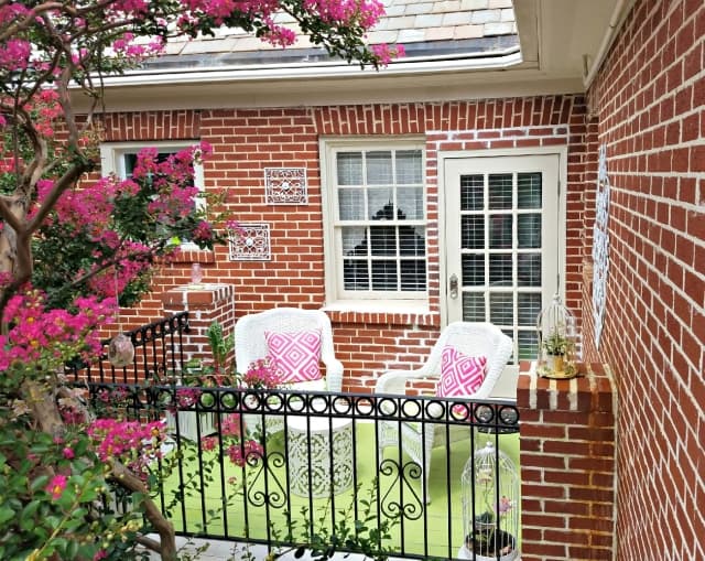 Balcony with two wicker chairs and pink cushions near crepe myrtle tree in bloom.