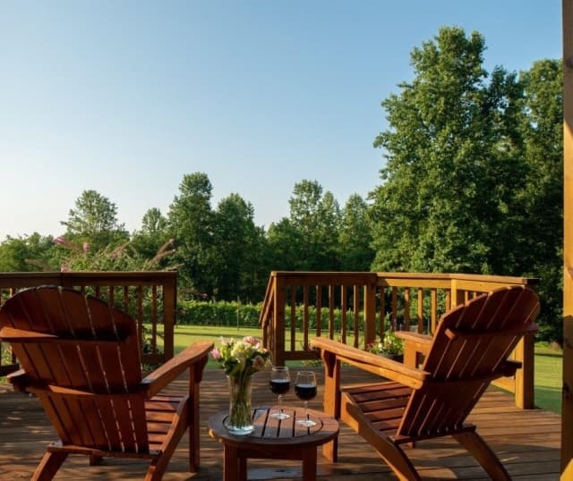 Arcady's Madison Suite deck with wood Adirondack chairs and a table overlooking lush green grass and trees