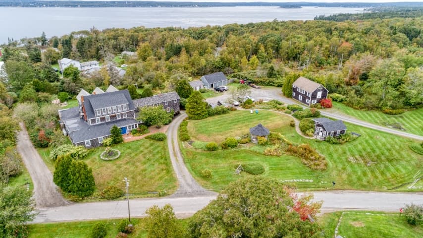 Ariel view of The Bradley Inn property, with green lawns, circular driveway, multiple rustic New England style buildings and a view of John's Bay in the distance.