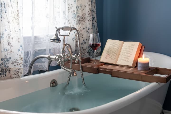 A book and a glass of wine on a tray over a bathtub at a bed and breakfast in Hershey, PA