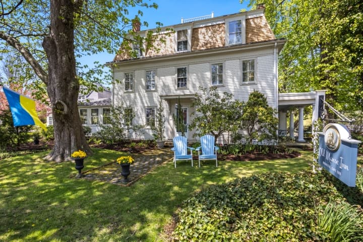 Classic New England-style inn with white clapboard siding, Adirondack chairs on a manicured lawn, and a welcoming sign that reads “Old Manse Inn – Brewster, Cape Cod.”