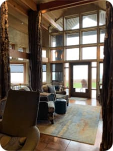 A gathering space with floor to ceiling windows and two armchairs next to a door