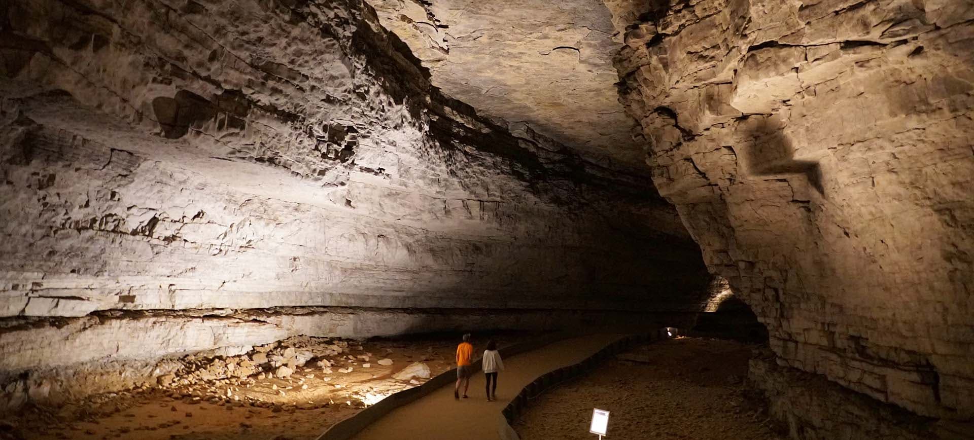 Walking path inside of Mammoth Cave with two people on a pathway in a large cavern